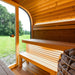 Wooden sauna interior with bench and basket of stones, surrounded by glass windows overlooking greenery.